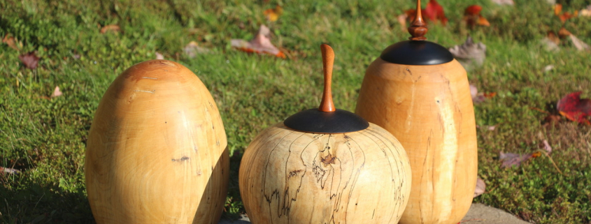 Trois urnes en bois posées sur une pierre dans un paysage d'automne.